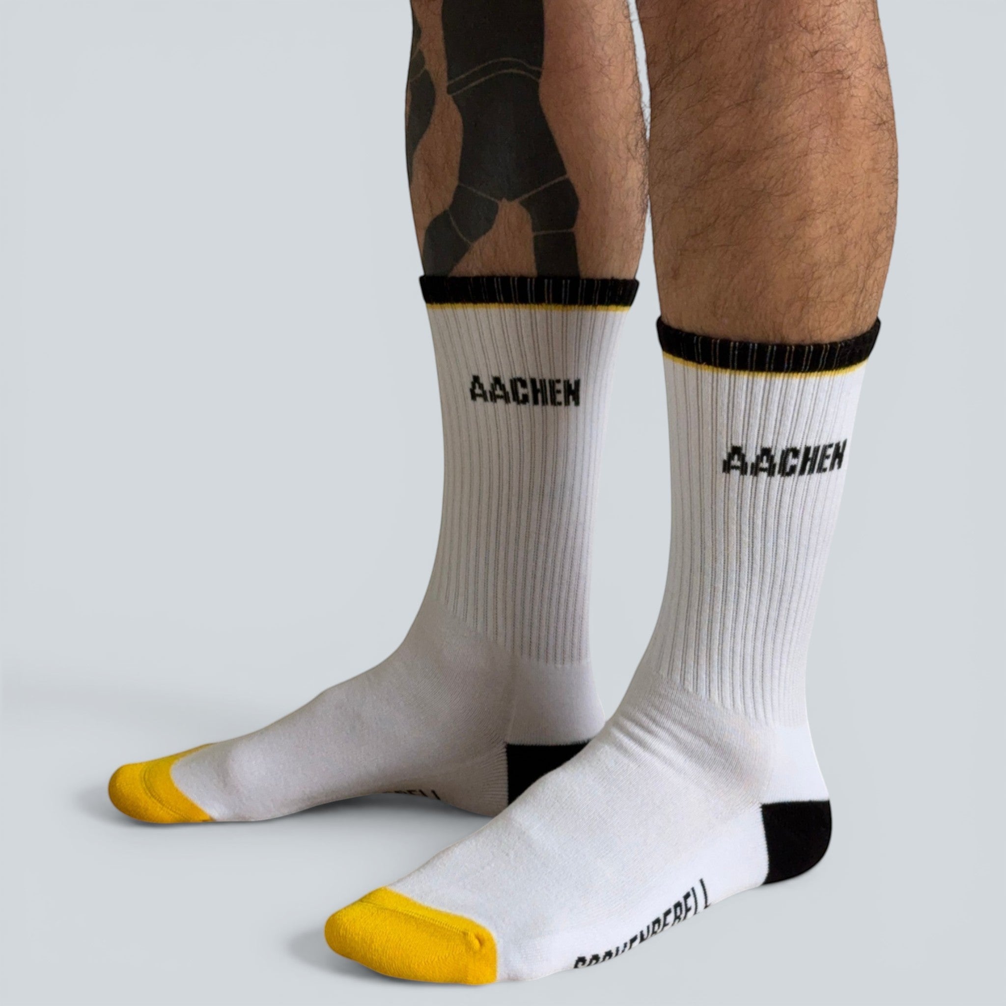 SOCKENREBELL Aachen white crew socks with black and yellow accents, featuring "AACHEN" text.