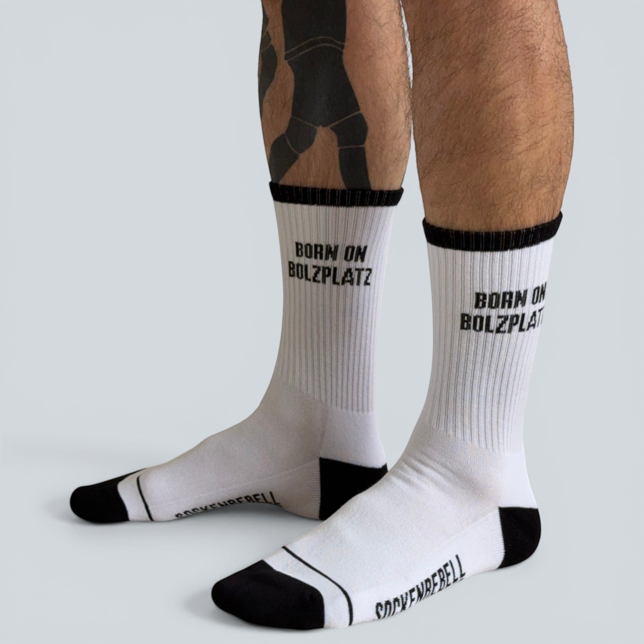 SOCKENREBELL white crew socks with black trim and toe, featuring "BORN ON BOLZPLATZ" text.
