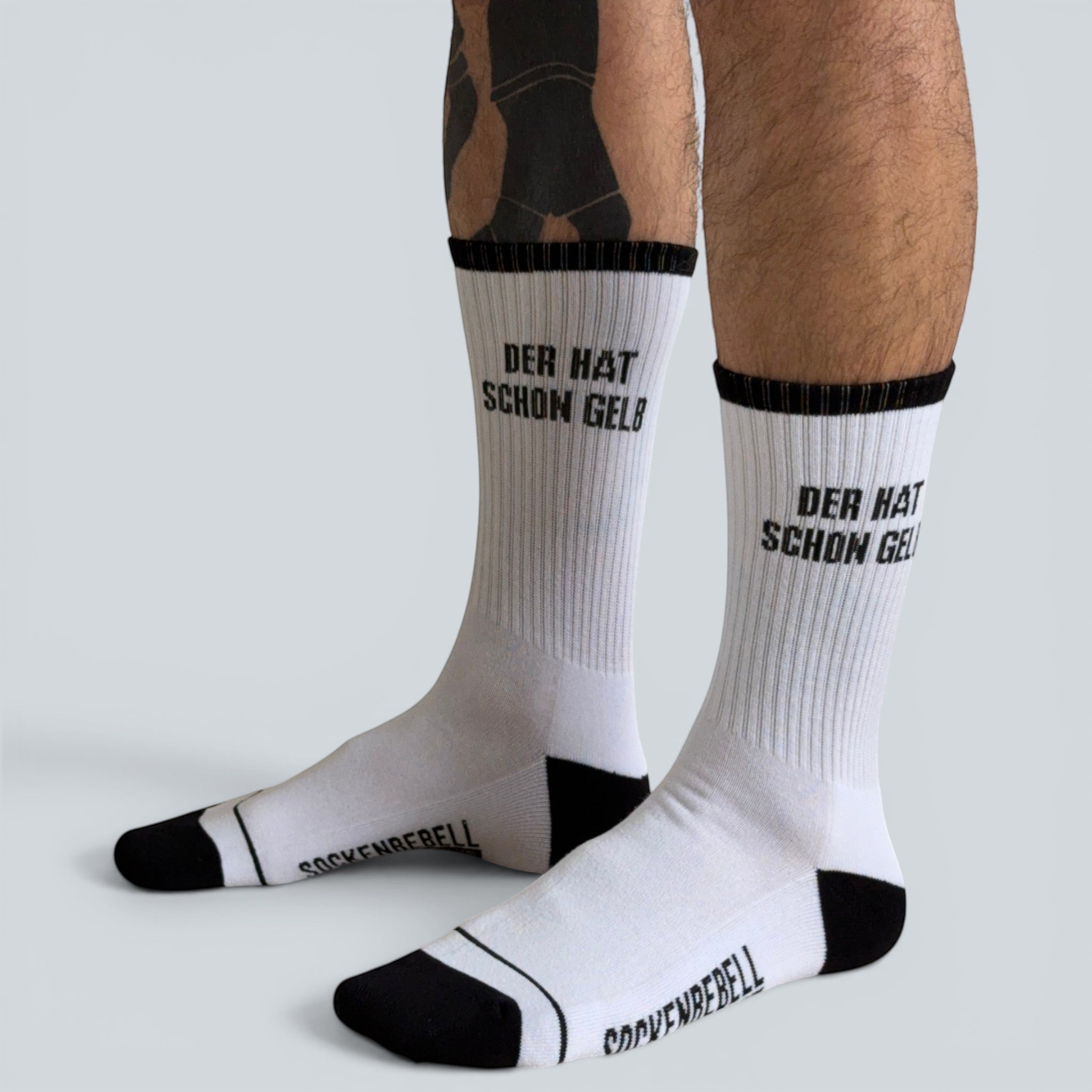 SOCKENREBELL white crew socks with black toe and heel, featuring "DER HAT SCHON GELB" text.