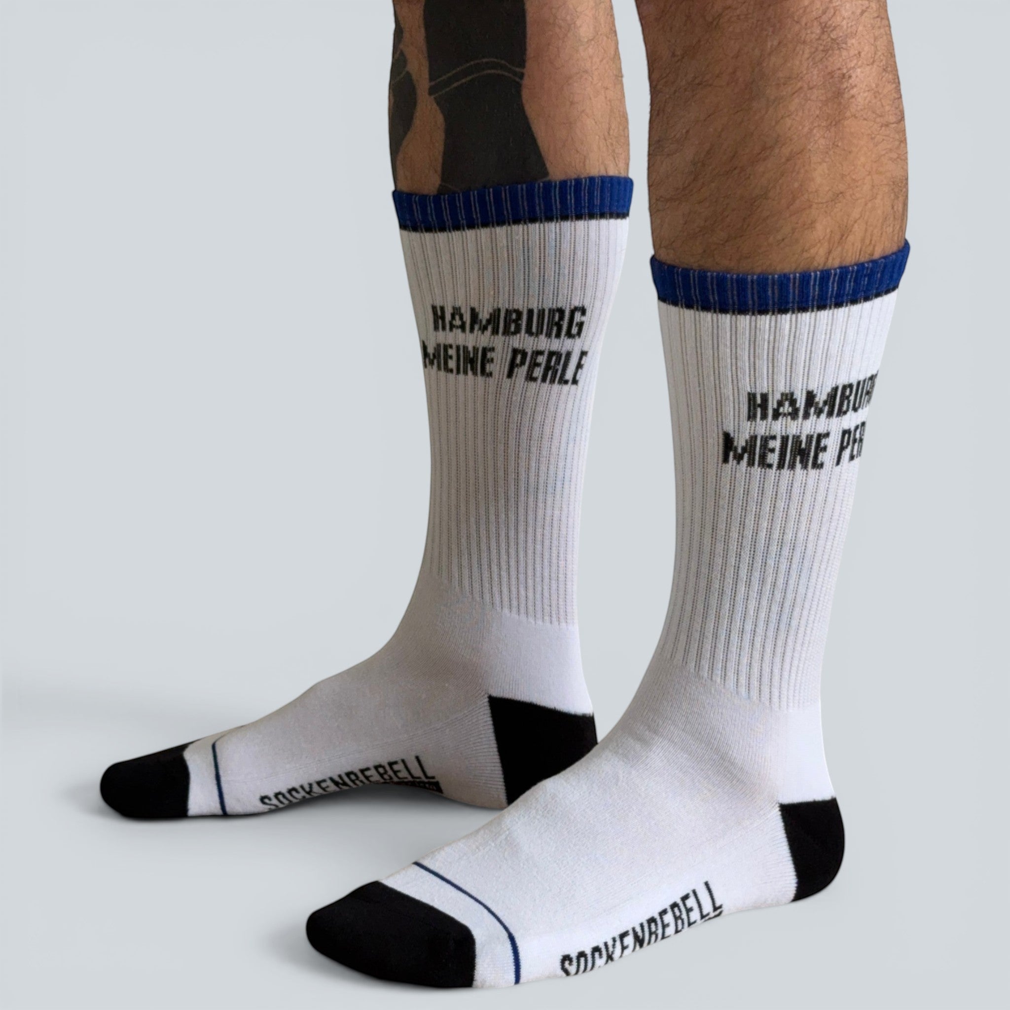 SOCKENREBELL white crew socks with blue trim and black toe/heel, featuring "HAMBURG MEINE PERLE" text.