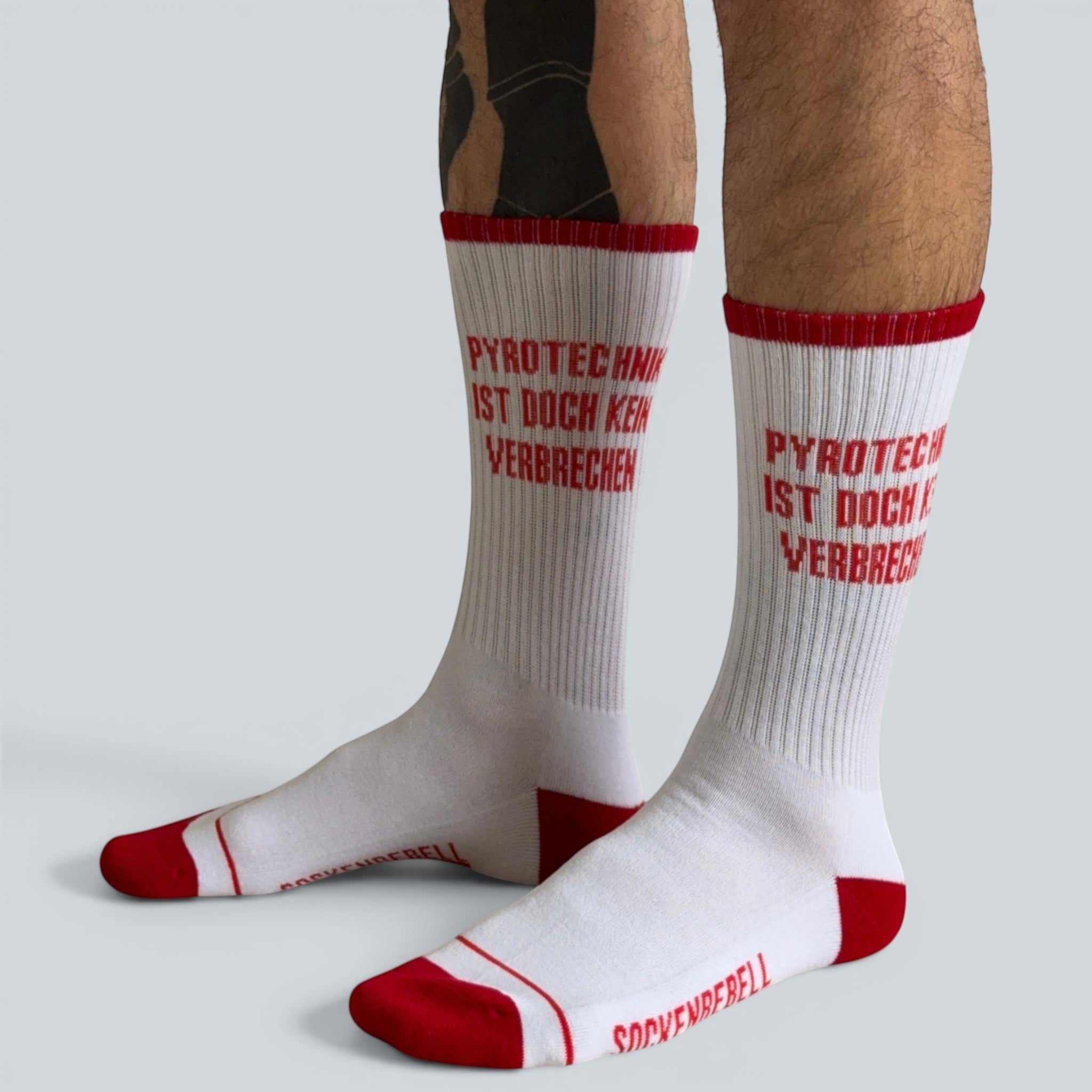 SOCKENREBELL white crew socks with red trim and red toe/heel. Features bold red text "PYROTECHNIK IST DOCH KEIN VERBRECHEN".