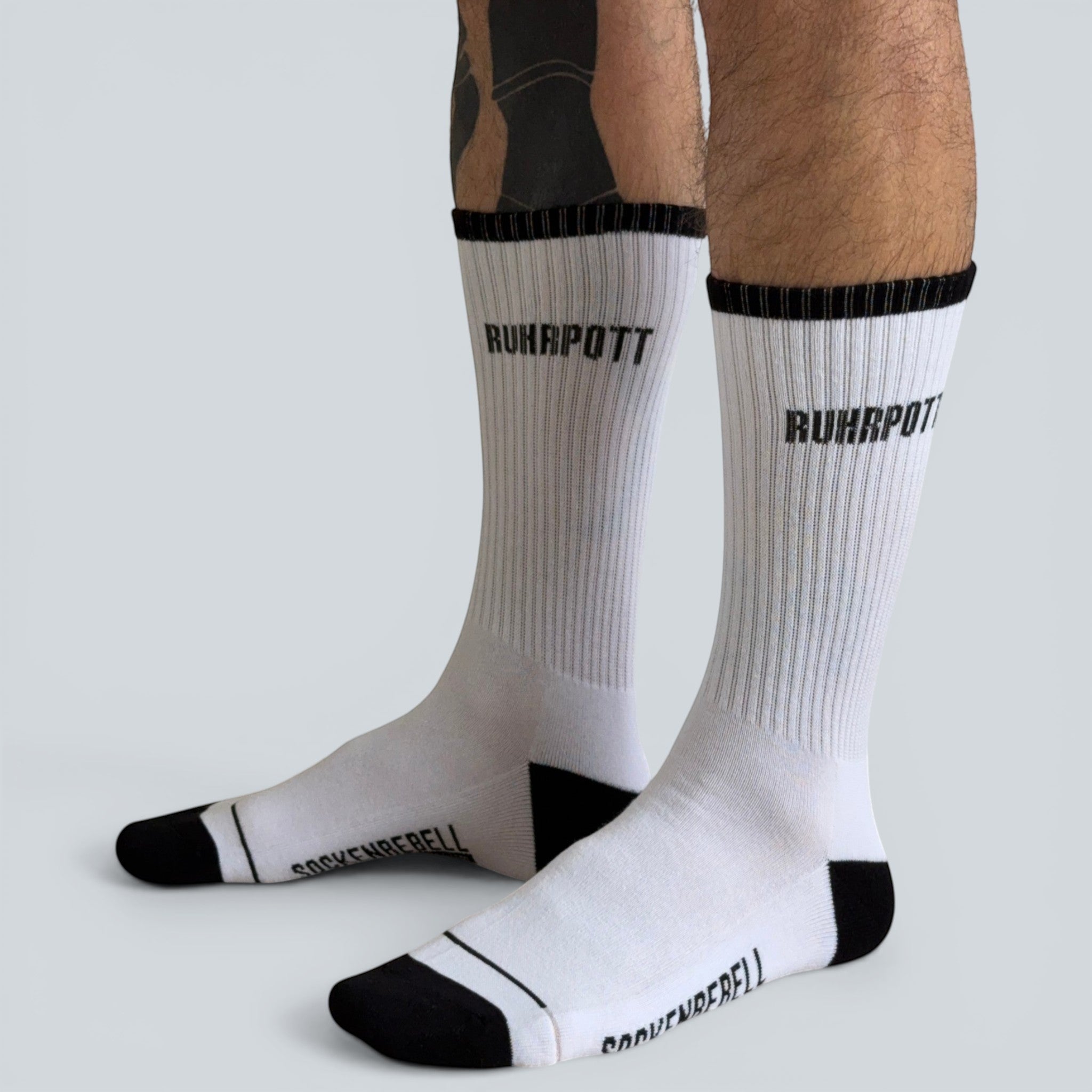 SOCKENREBELL white crew socks with black toe and heel, featuring "RUHRPOTT" text on the calf and "SOCKENREBELL" on the foot.